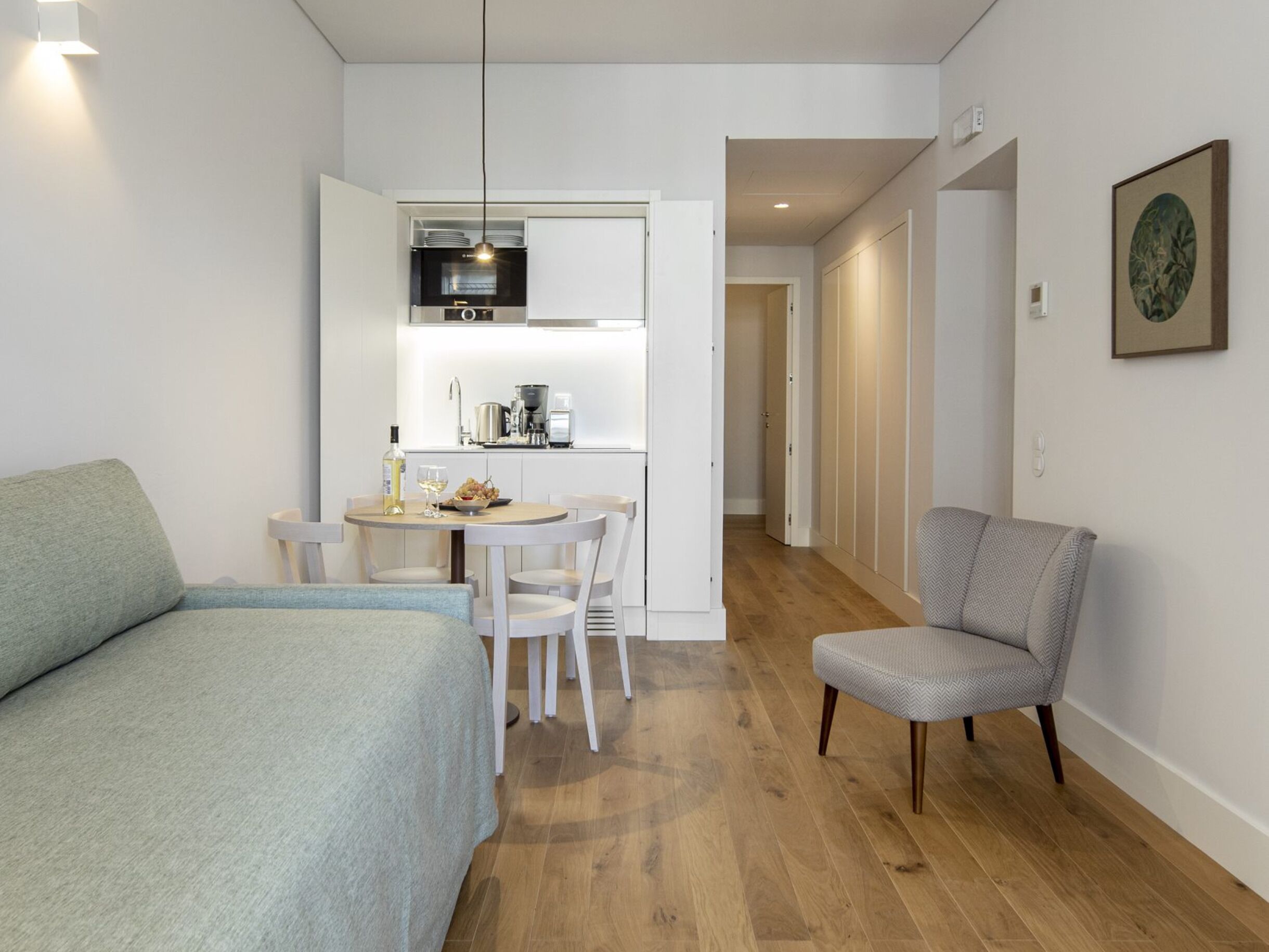 Una habitación compacta con cama, una mesa de comedor con sillas, una kitchenette y un sillón.