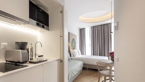 A compact hotel room with a kitchenette, a bed, a small dining area, and a view of the cityscape. - LSA Madalena by Numa (Lisbon)