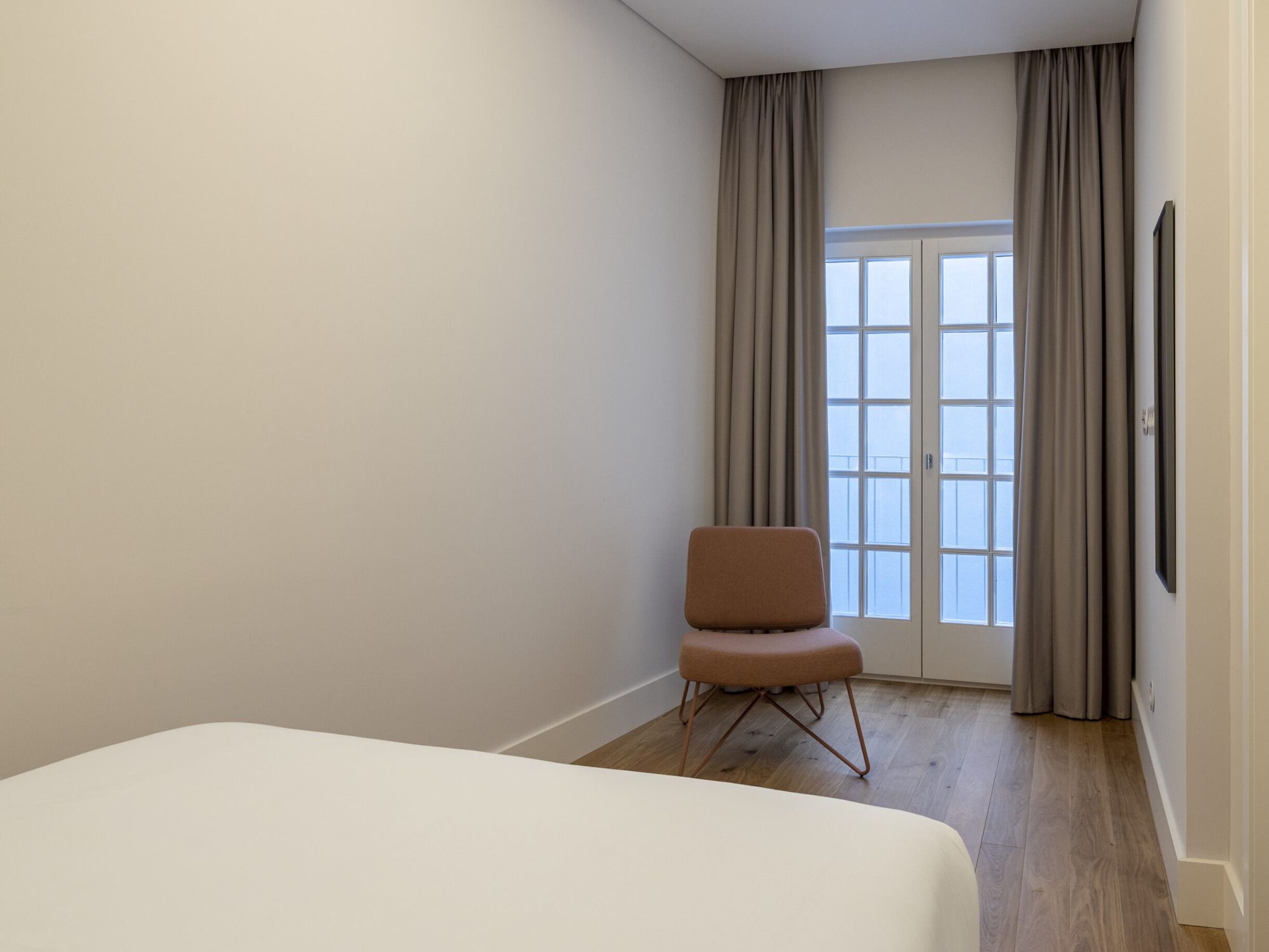 Una habitación de hotel con cama, una silla, ventana con cortinas y puerta.
