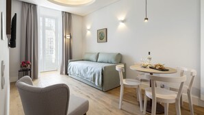 A modern living room with a sofa, a dining table with chairs, a TV mounted on the wall, and a window with curtains. - LSA Madalena by Numa (Lisbon)