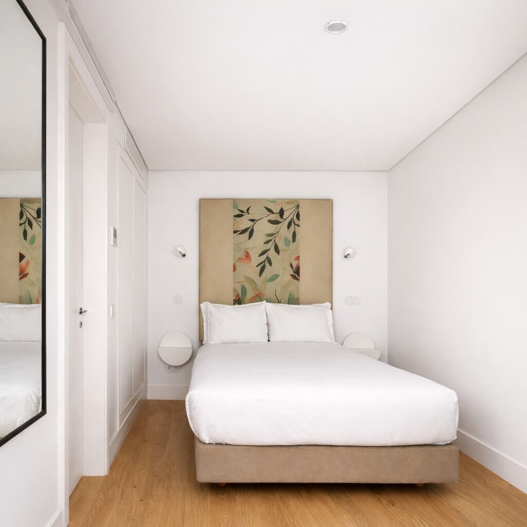 Una camera da letto con un letto, una testiera con motivo a foglia, lampade sui comodini e un pavimento in legno.