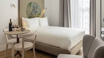 Une chambre d’hôtel avec un lit, une table ronde entourée de chaises, une bouteille de vin et un tableau accroché au mur.