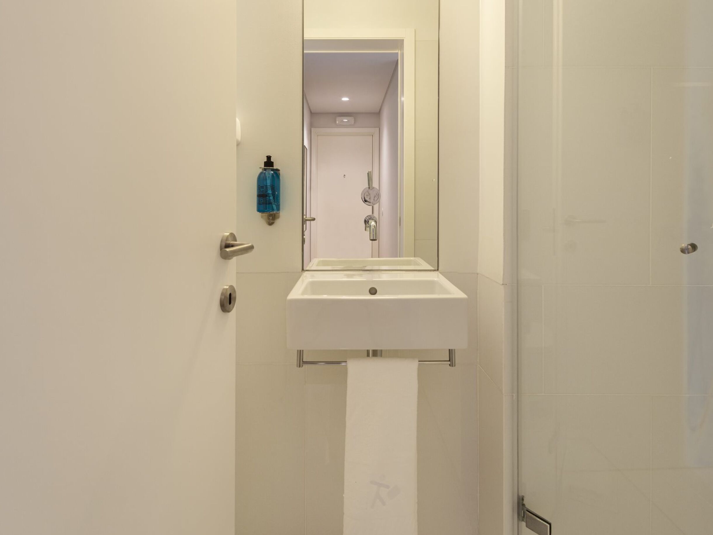 Une salle de bain avec un lavabo blanc, un miroir, un distributeur de serviettes et un espace douche.