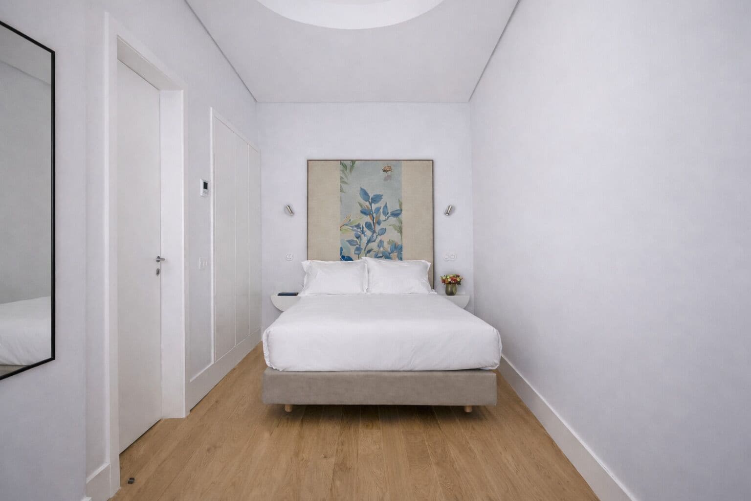 A bedroom with a bed, a nightstand, a wall-mounted artwork, and a door.