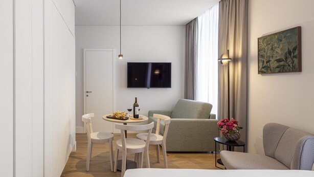 A modern hotel room with a bed, a dining area with chairs and a table, a sofa, and a TV mounted on the wall. - LSA Madalena by Numa (Lisbon)