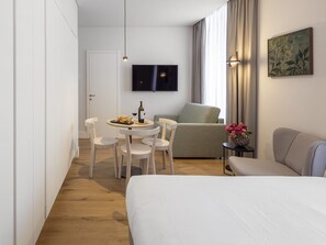 A modern hotel room with a bed, a dining area with chairs and a table, a sofa, and a TV mounted on the wall. - LSA Madalena by Numa (Lisbon)