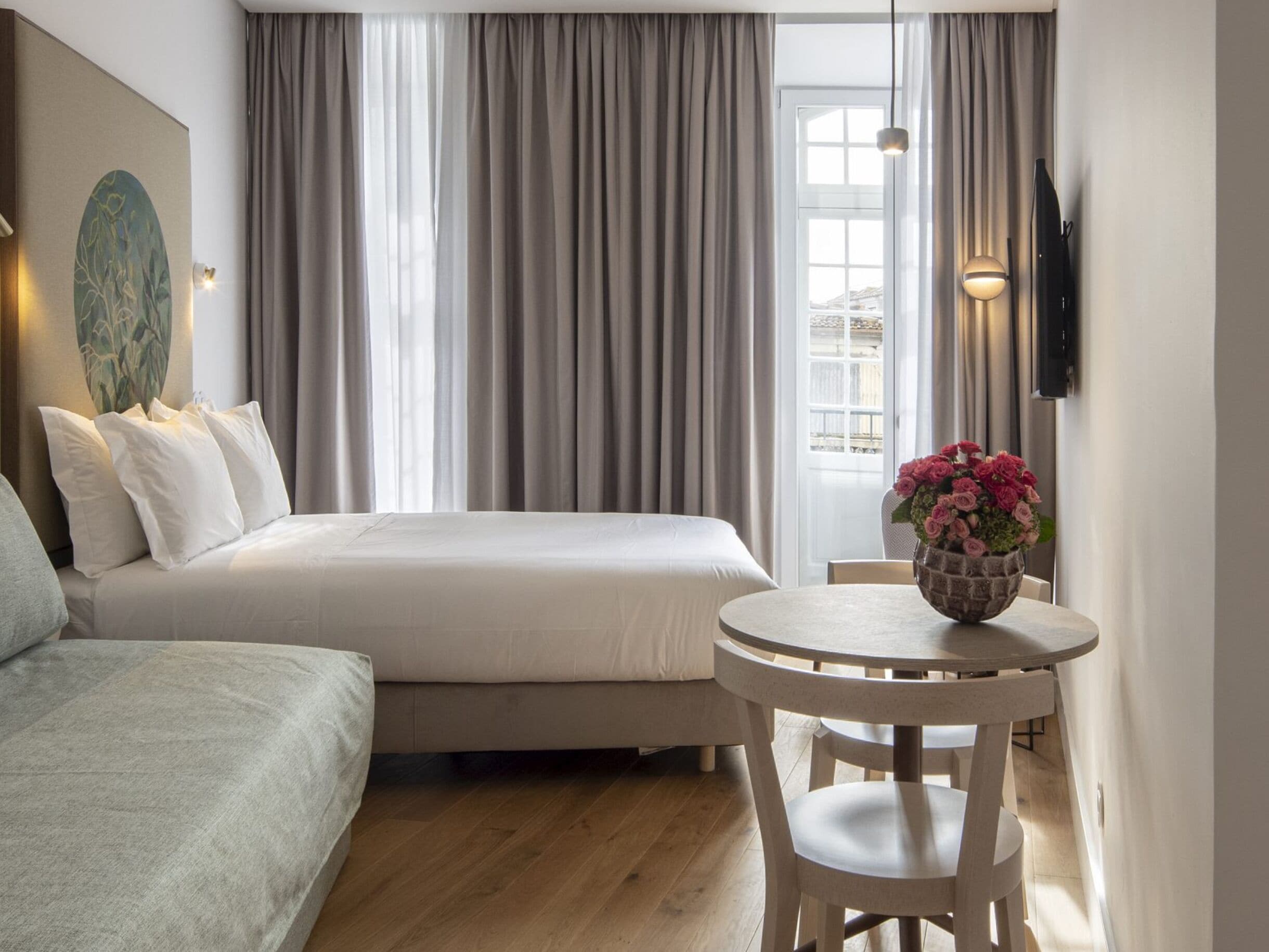 A hotel room with a bed, a seating area with a table, and a large window with curtains.