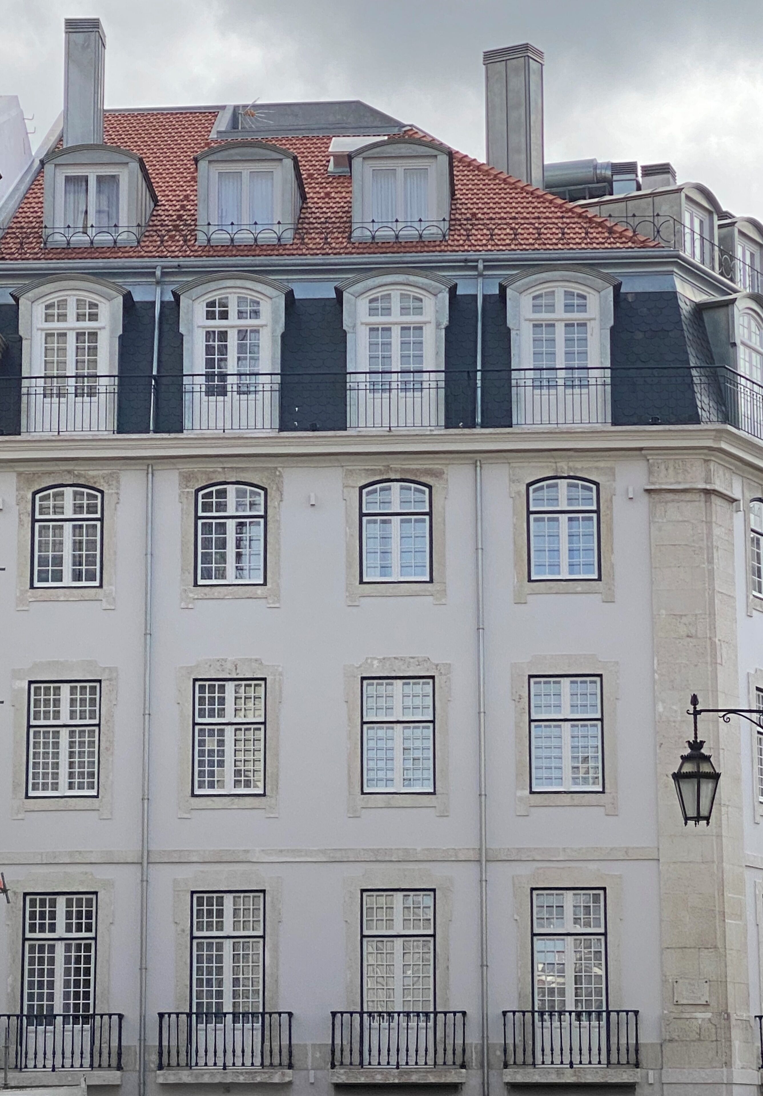 A multi-story building with a red-tiled roof, white-framed windows, and a black metal railing on the balconies.