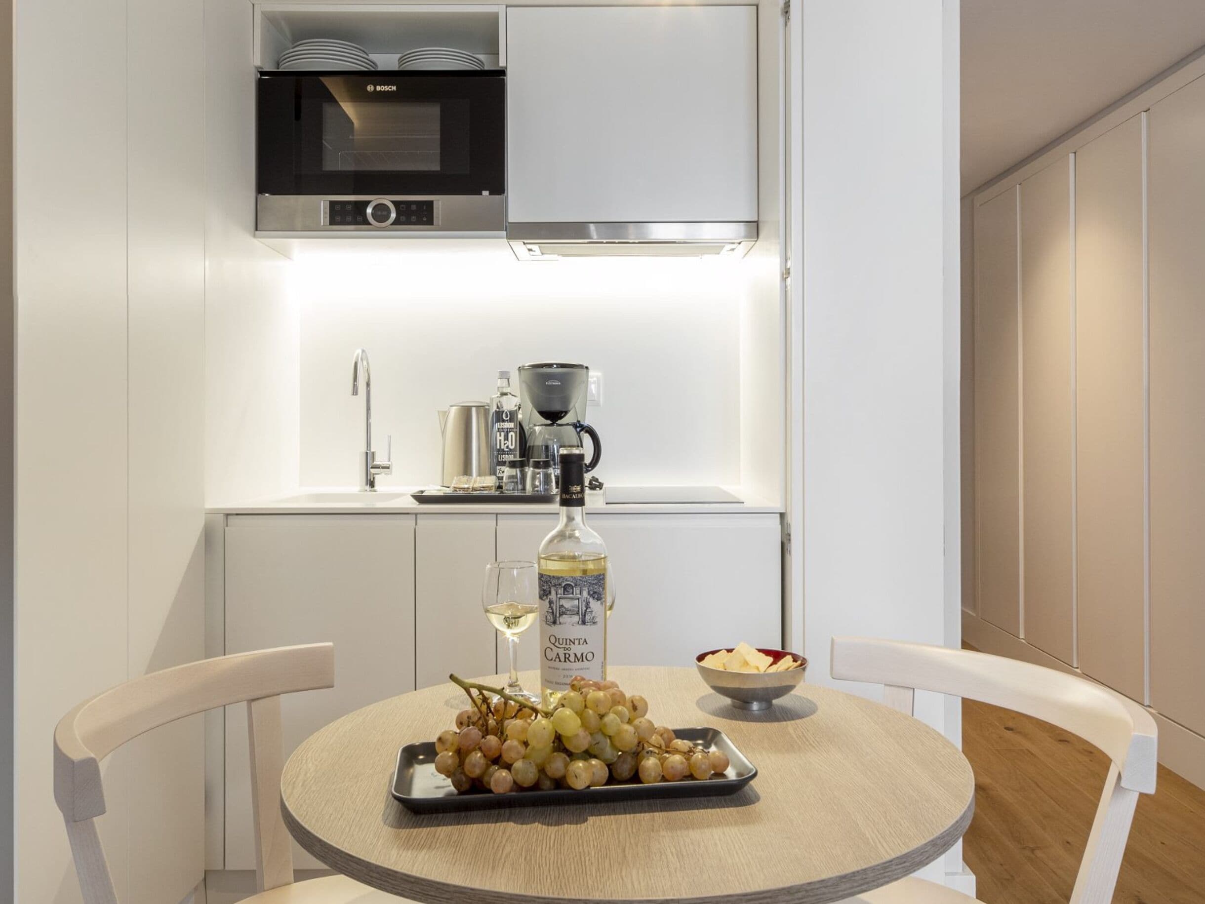 Una cocina compacta con un microondas Bosch, una cafetera y una botella de vino Quinta Carmo sobre la encimera.