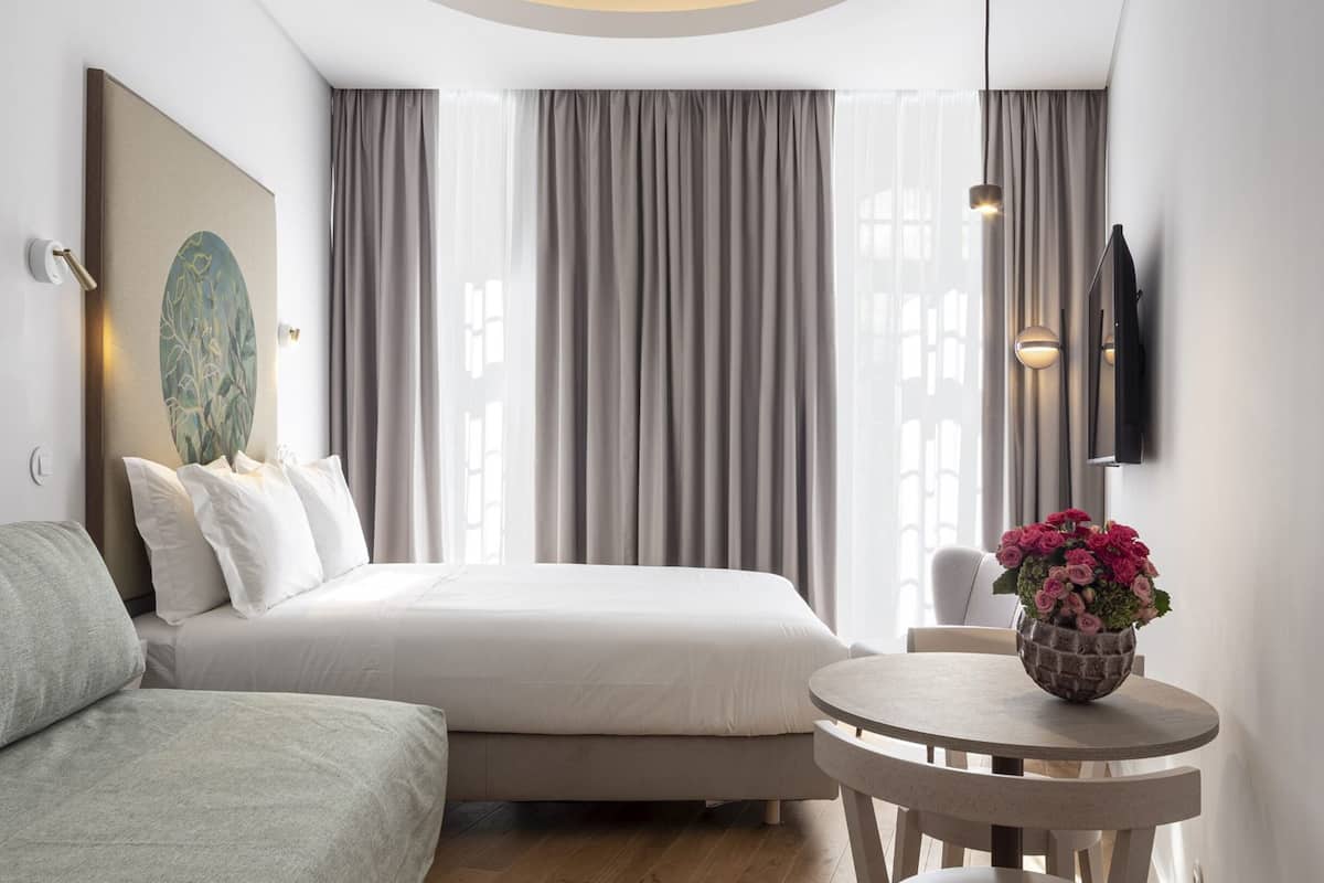 A modern hotel room with a bed, a round table, and a wall-mounted TV.
