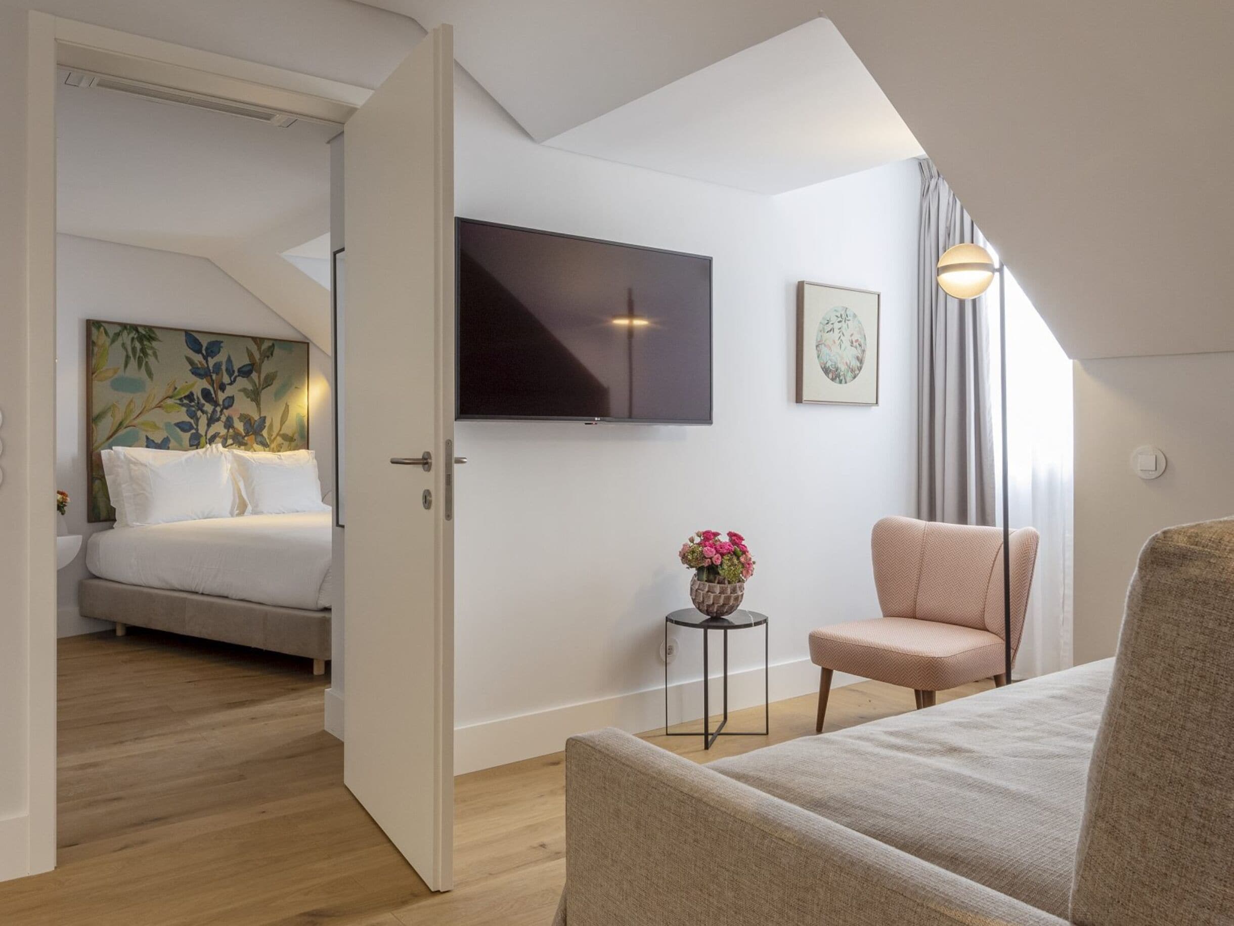 A modern bedroom with a bed, a TV mounted on the wall, a small table with flowers, and a chair.