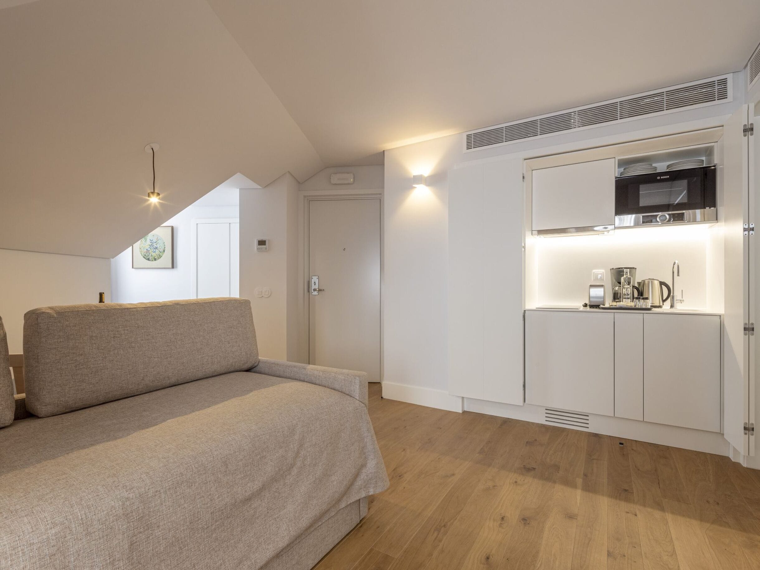A bedroom with a bed, a kitchenette with a microwave, and a door leading to another room.
