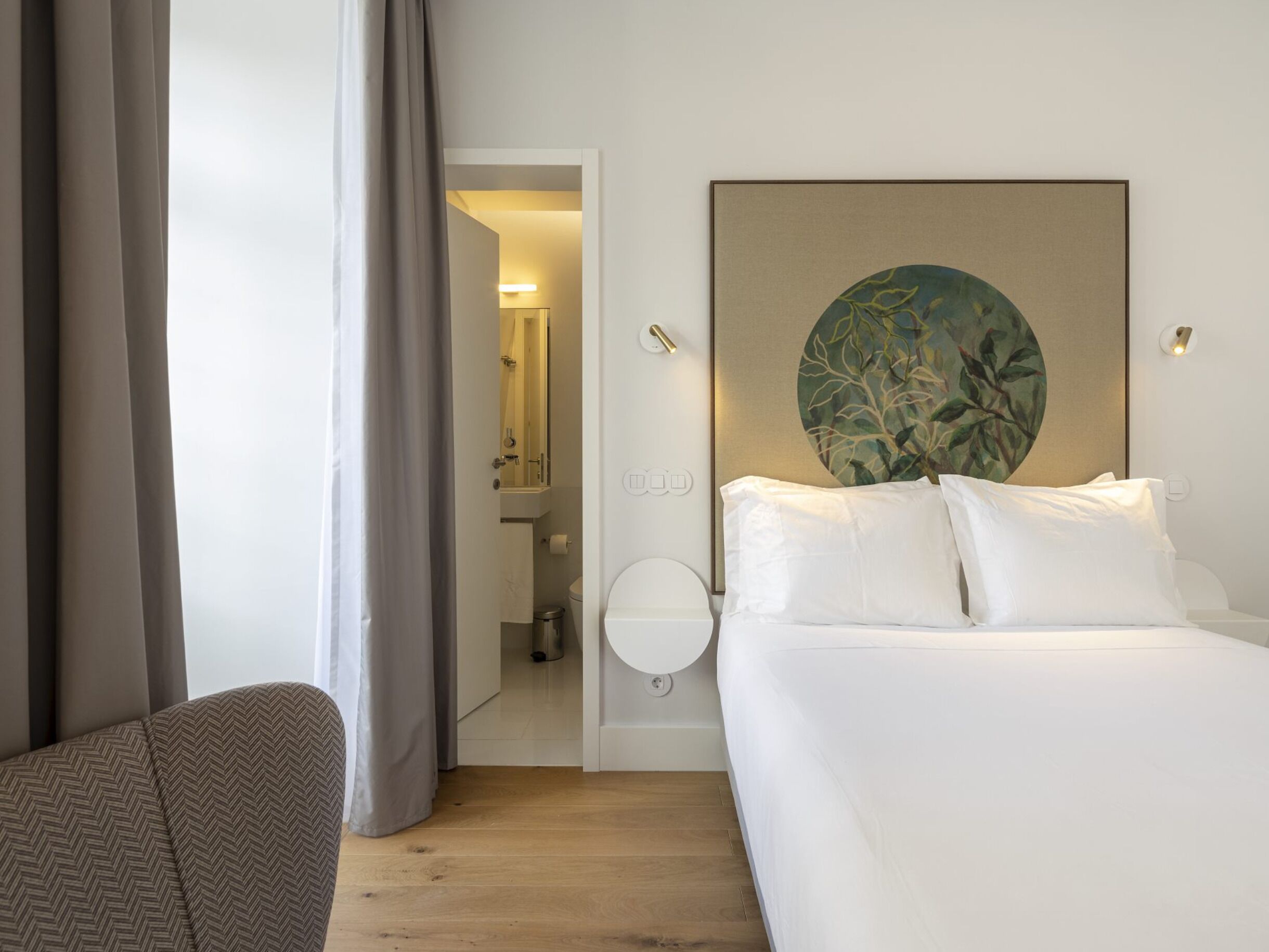 Habitación de hotel con cama, una silla, un adorno circular en la pared y vistas al baño.