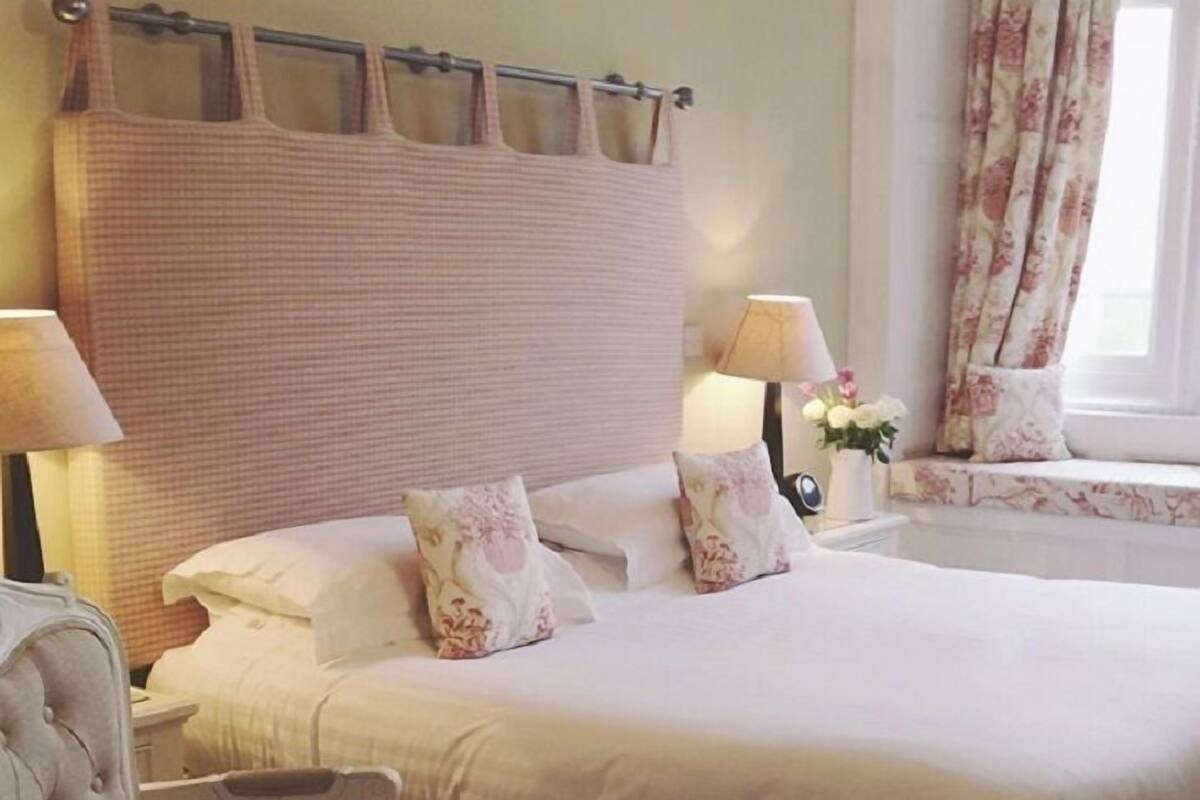 A hotel room with a large bed, two bedside tables with lamps, a chair, and a window with curtains.