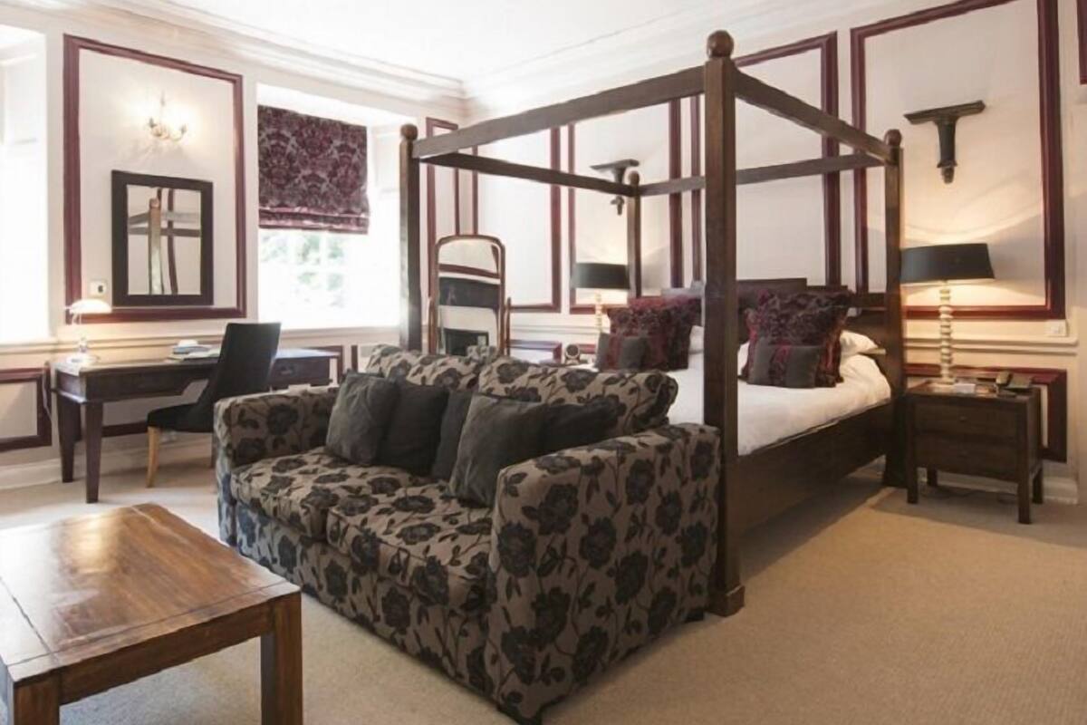 A room with a four-poster bed, a sofa, a desk, and a chair.