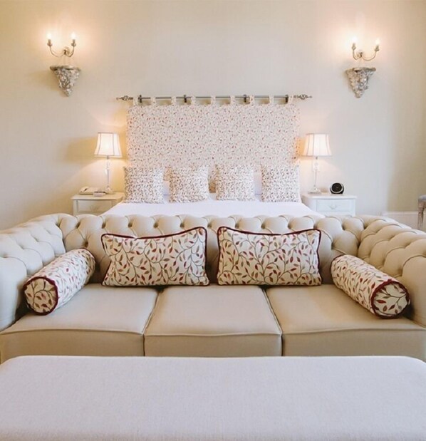 A bedroom with a tufted headboard, a large bed with multiple pillows, two bedside tables with lamps, and wall sconces. - Langdon Court Hotel (Plymouth)