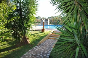 A stone pathway leading to a swimming pool surrounded by lush greenery. - Pousada Recanto dos Pássaros (Bonito)