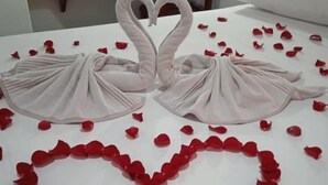 Una cama con un arreglo de pétalos de rosa en forma de corazón y toallas dobladas como cisnes.