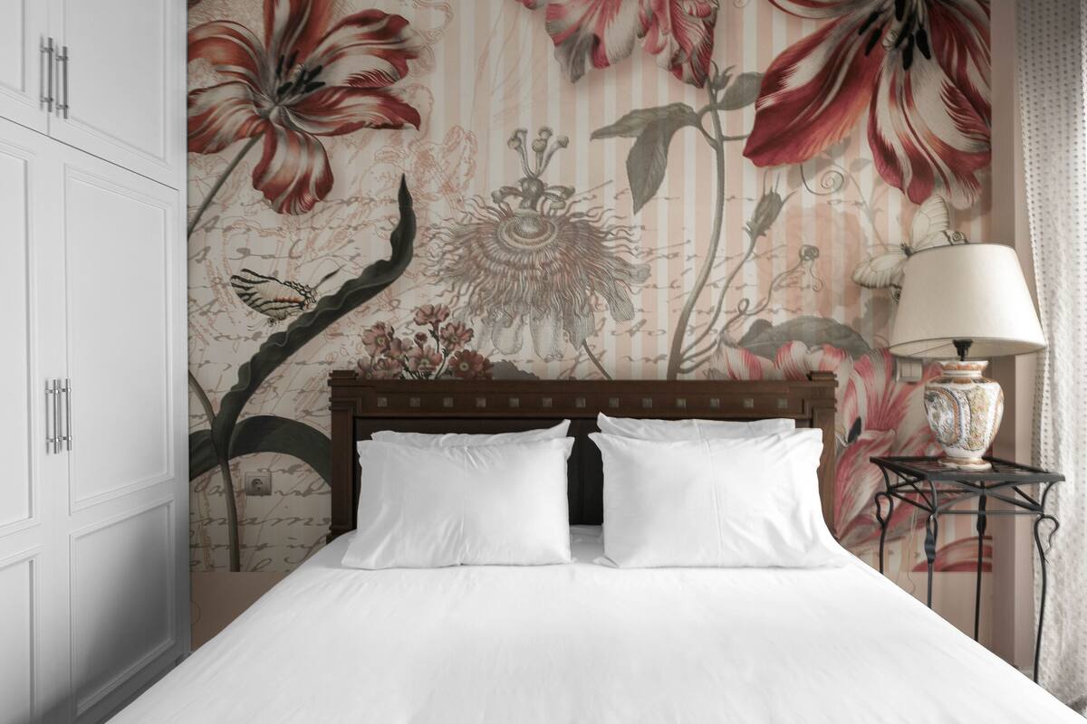 Una habitación de hotel con una cama grande, cabecera de madera y diseño de papel tapiz floral.