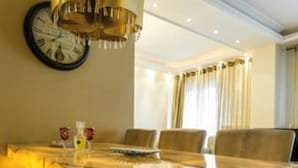 A dining area with a long table and multiple chairs, a clock on the wall, and a chandelier. - Aristotelous Grand View (Thessaloniki)