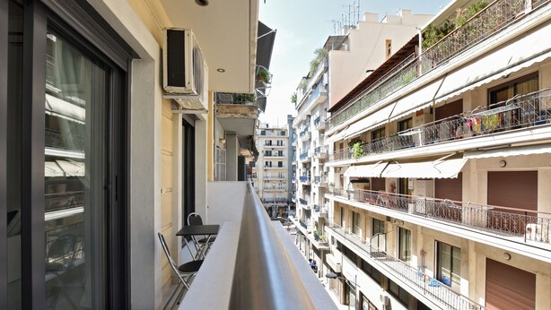 Une rue étroite en milieu urbain, bordée d’immeubles à plusieurs étages et agrémentée de balcons, avec un ciel dégagé.
