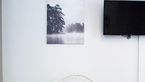 A white chair with a patterned cushion in a room with a white wall, a black TV mounted on it, and a framed picture above the TV. - Downtown Penthouse Thessaloniki (Thessaloniki)