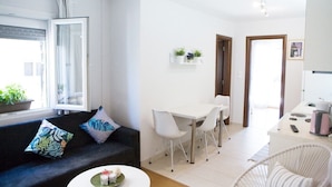 A modern living room with a sofa, a dining table with chairs, a kitchen area with a coffee machine, and a view of the outside. - Downtown Penthouse Thessaloniki (Thessaloniki)