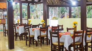 Un restaurante con mesas y sillas de madera, cubiertas con manteles blancos y decorado con flores amarillas.