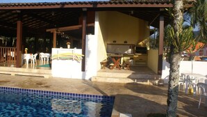 A covered outdoor area with a pool, a barbecue setup, and outdoor seating. - Pousada A Cor do Sol (Ubatuba)