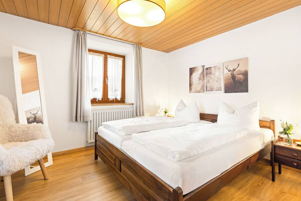 Ein Schlafzimmer mit zwei Betten, Holzboden, einem Fenster mit Vorhängen und Wandbildern.