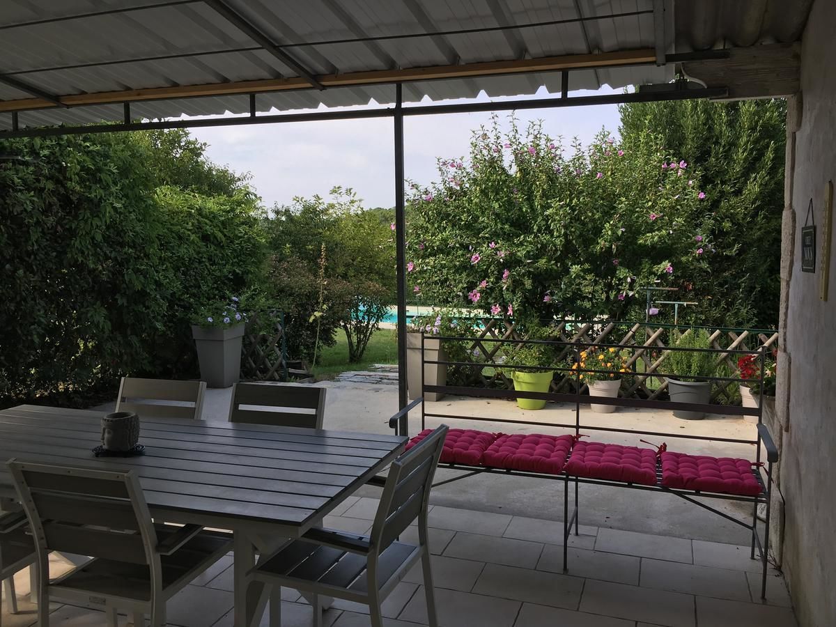 Une terrasse extérieure avec une table et des chaises, entourée de plantes en pot et d’une clôture en bois.