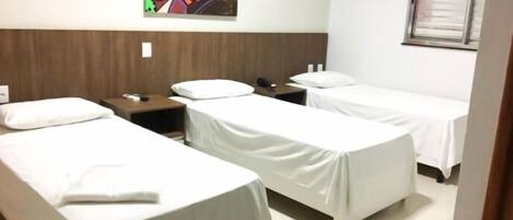 Habitación de hotel con dos camas individuales, cabecero de madera, mesita de noche con lámpara, un cuadro en la pared y una ventana con persianas.