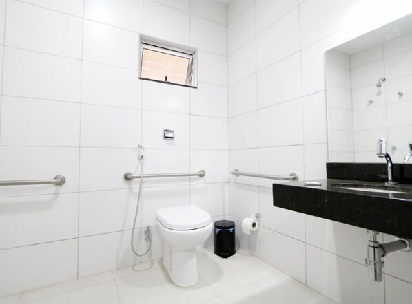 Un baño moderno con azulejos blancos, un inodoro, un bidé, un cubo de basura y un lavabo con espejo.