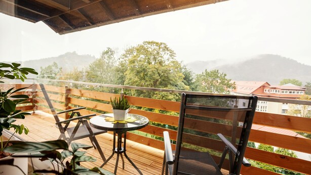 Eine Holzterrasse mit Tisch und Stühlen, einem Blumentopf und Blick auf Berge und Gebäude in der Ferne.