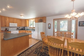 A modern kitchen with wooden cabinets, a central island, and a dining area with a chandelier. - Dolphin House (Haines)