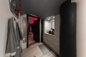 A hallway with a wooden floor, a black wall, and a window with a coffee machine.