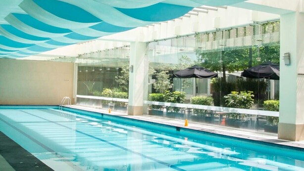 Une piscine à l’eau claire, entourée de murs de verre et surmontée d’un plafond orné de motifs de vagues bleues.