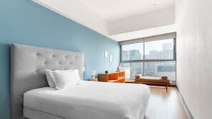 Une chambre moderne avec un grand lit, une table de chevet, une petite table et une fenêtre donnant sur la ville.