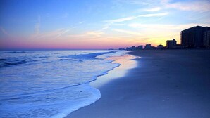 A beach with a calm sea and a city skyline in the background.