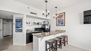 A modern kitchen with a central island, bar stools, and a large painting.