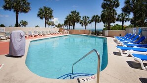 A pool with lounge chairs and palm trees, a lifeguard tower, and a clear view of the ocean.