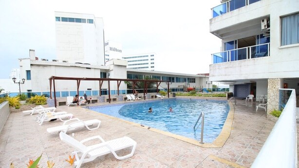 En pool på taket med solstolar, ett avskärmat sittområde och utsikt över Hiltonhotellets byggnad i bakgrunden.