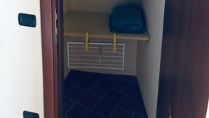 Een kleine inloopkast met een bed bovenop, een kledingroede en een blauw kledingstuk op een plank.