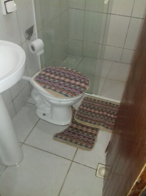 Un baño con inodoro, un rollo de papel higiénico y un tapete estampado en el suelo.