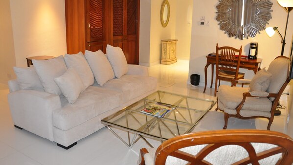 Una sala de estar con un sofá blanco, una mesa de centro de vidrio y muebles de madera.