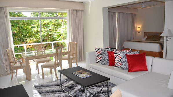 A modern hotel room with a balcony, a dining area, a sofa with patterned cushions, and a bed with a headboard. - Pegasus Hotel By the Waterfront (Georgetown)