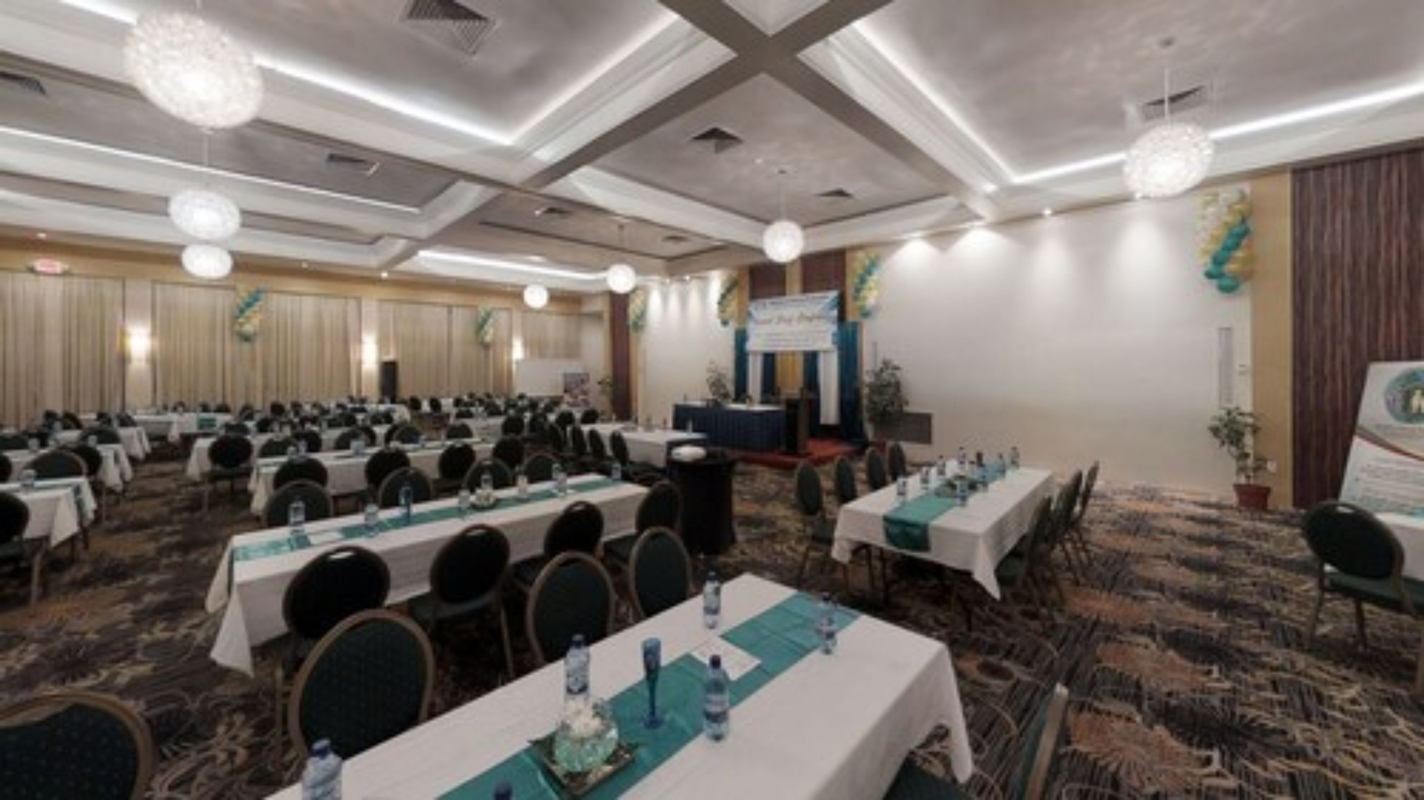 A conference room with multiple tables and chairs, a stage with a podium, and a banner.