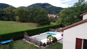 A residential area with a swimming pool, a well-maintained lawn, and a view of a forested hill. - Chambres des Arrys (Bas-en-Basset)