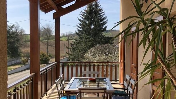 A covered outdoor patio with a glass table and chairs, a wooden deck, and a view of a tree and landscape. - Chambres des Arrys (Bas-en-Basset)