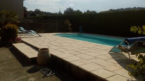 A swimming pool with a tiled deck, lounge chairs, and a large planter. - Chambres des Arrys (Bas-en-Basset)